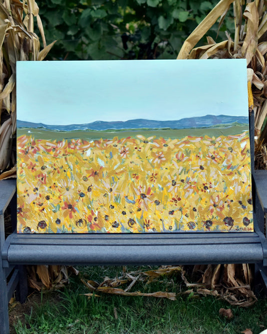 Bench with a painting of a field of flowers surrounded by pumpkins and corn stalks.