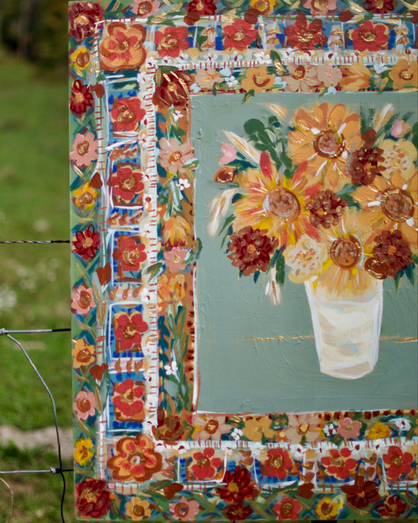 Decorative floral frame with a painting of flowers inside, set against a natural background.